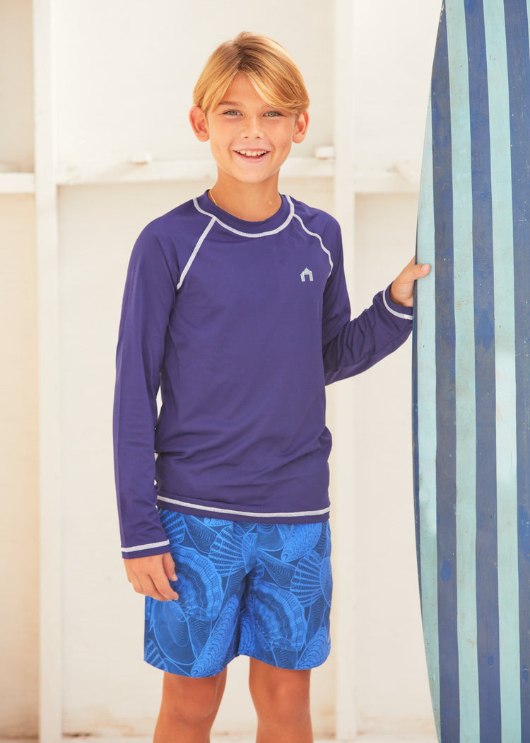 Boy wearing the Cabana Life San Sebastian Shell Boys Swim Trunks posing with his surfboard. 