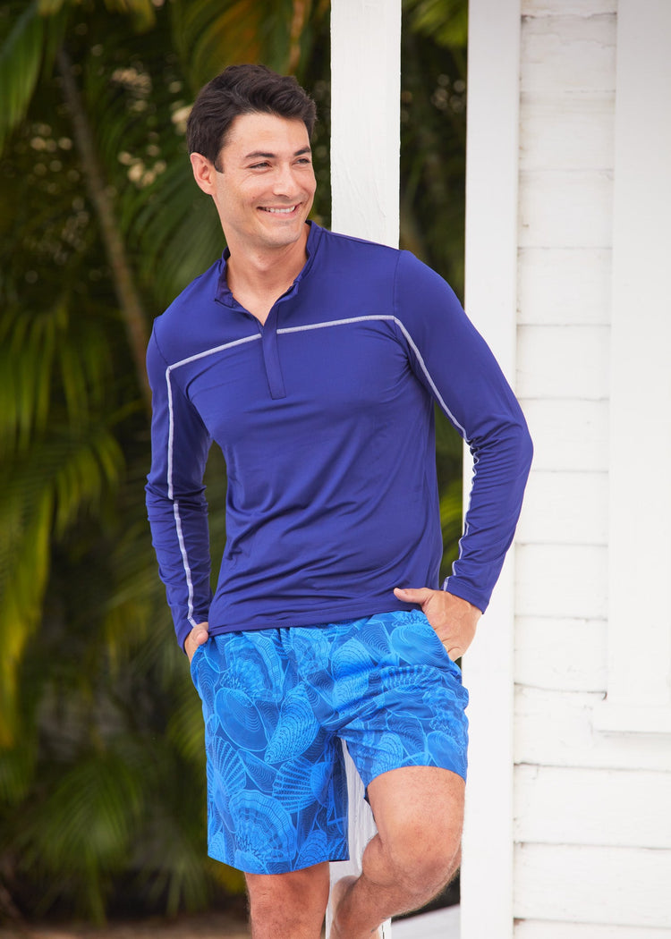 Man standing in front of a beach side cottage wearing the blue patterned and sun protective Cabana Life San Sebastian Shell Men's Swim Trunk.