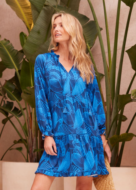Woman wearing the blue patterned sun protective Cabana Life San Sebastian Tiered Ruffle Dress while looking over her shoulder.