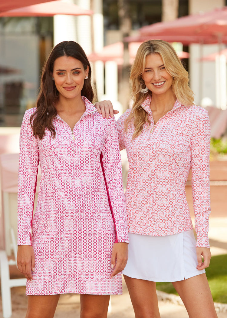 Blonde woman wearing the sun protective Algarve Sport Zip Polo with the sun protectivwe White Classic Swim Skirt with palm trees and pink beach umbrellas in background next to brunette woman wearing the sun protective Algarve Sport Zip Dress.