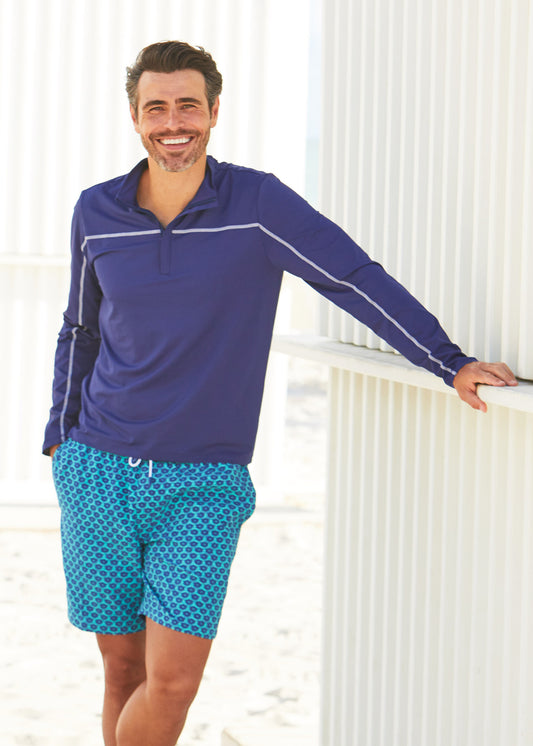 Man leaning against beach shack wearing Cabana Life Navy Sport Zip Top with Aruba Blues Swim Trunks
