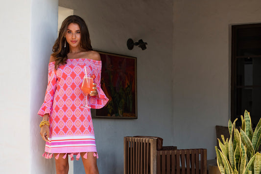 Woman wearing Coral Geo Off the Shoulder dress while holding a cocktail.