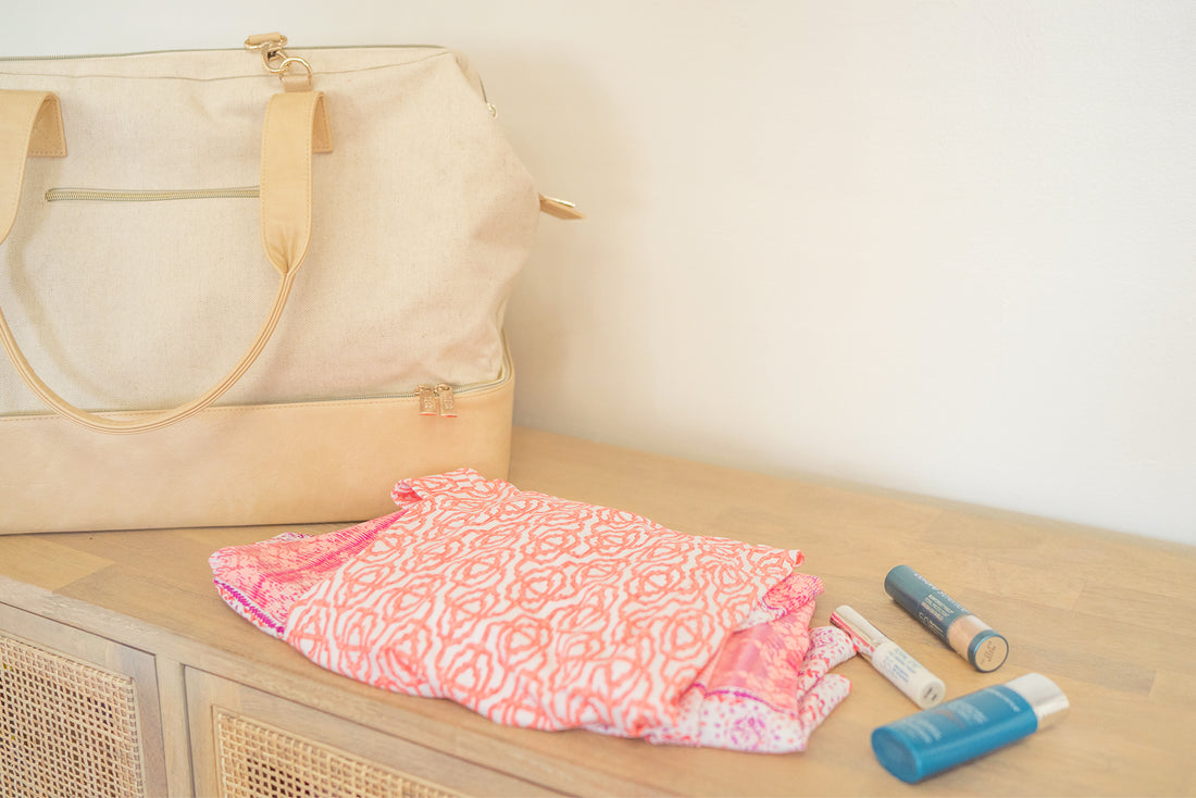 Cream colored Beis weekender bag on table top with Cabana Life Napa print and colorscience makeup items