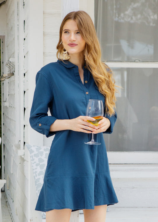 Woman in a blue dress holding a glass of wine outdoors.
