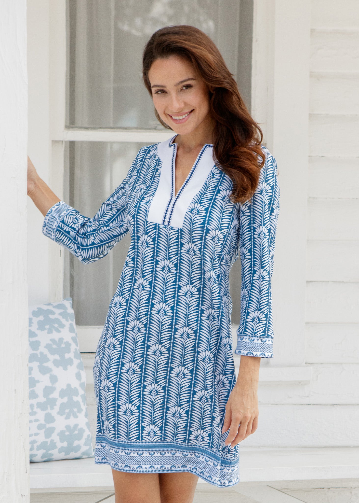 Woman wearing a blue and white patterned dress standing in front of a white door.