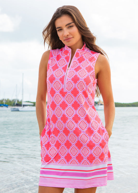 Woman wearing a pink patterned sleeveless dress by a body of water.
