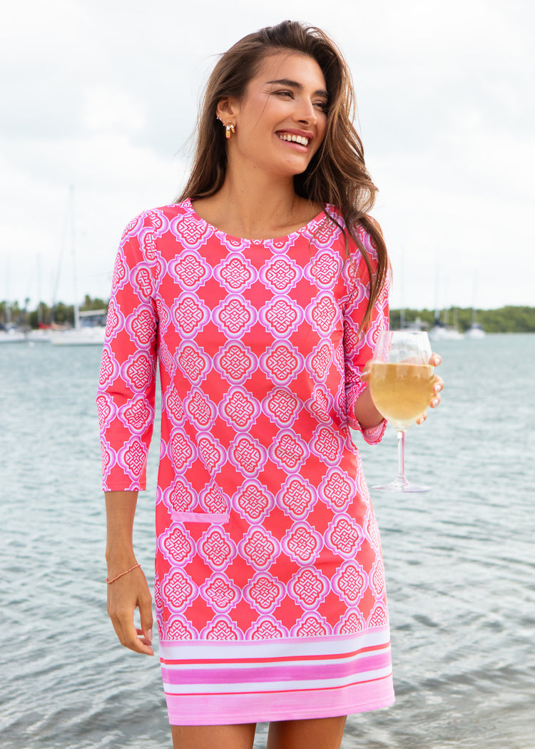 Woman in a pink patterned dress holding a glass of wine by a body of water.