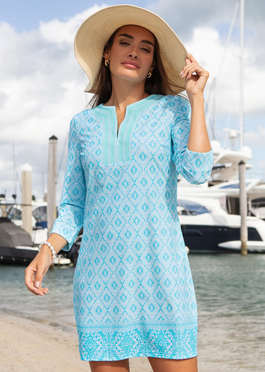 Woman in a light blue dress with a pattern, standing by a marina.