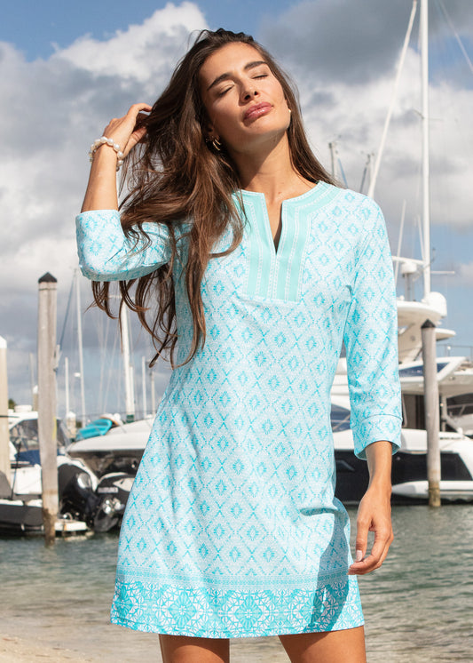 Woman wearing a light blue dress with a pattern standing by a marina.