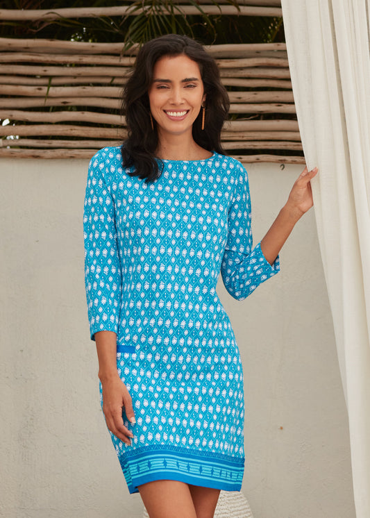 Woman wearing Palm Valley Cabana Shift Dress with one hand holding white curtain.