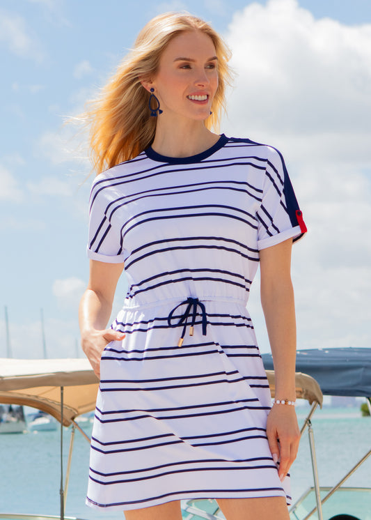 Woman wearing a white and navy striped dress with a blue sky and water background