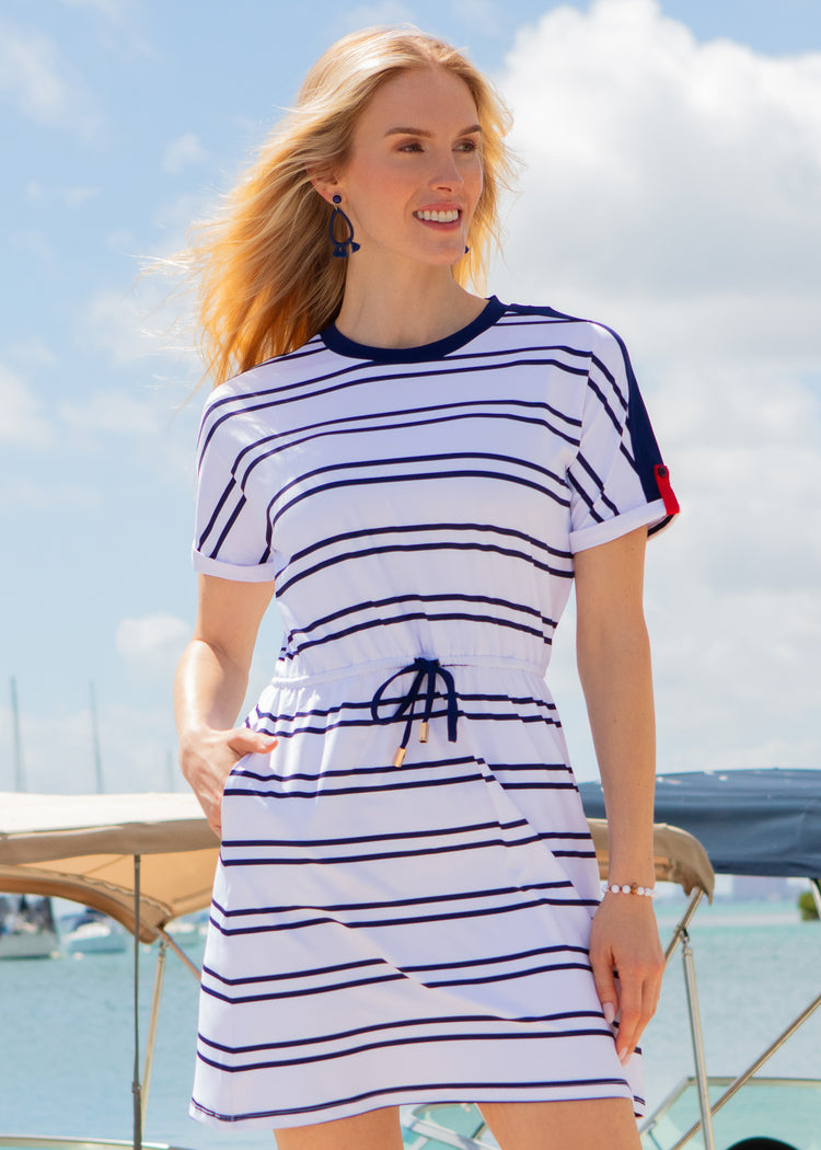 Woman wearing a white and navy striped dress with a blue sky and water background