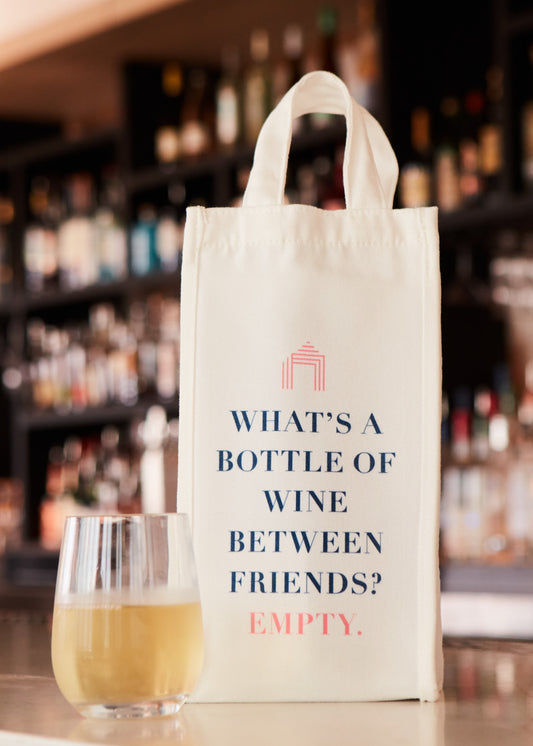 A white fabric Wine Tote Bag next to a glass of white wine on a bar counter.