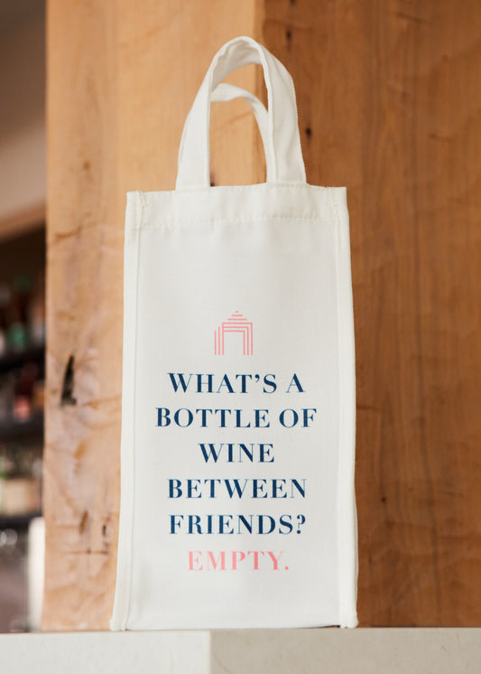 A white fabric Wine Tote Bag next to a glass of white wine on a counter.