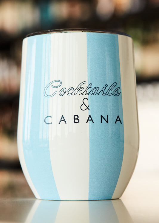 A Cocktails & Cabana Striped Stemless Wine Tumbler on white counter in front of a bar.