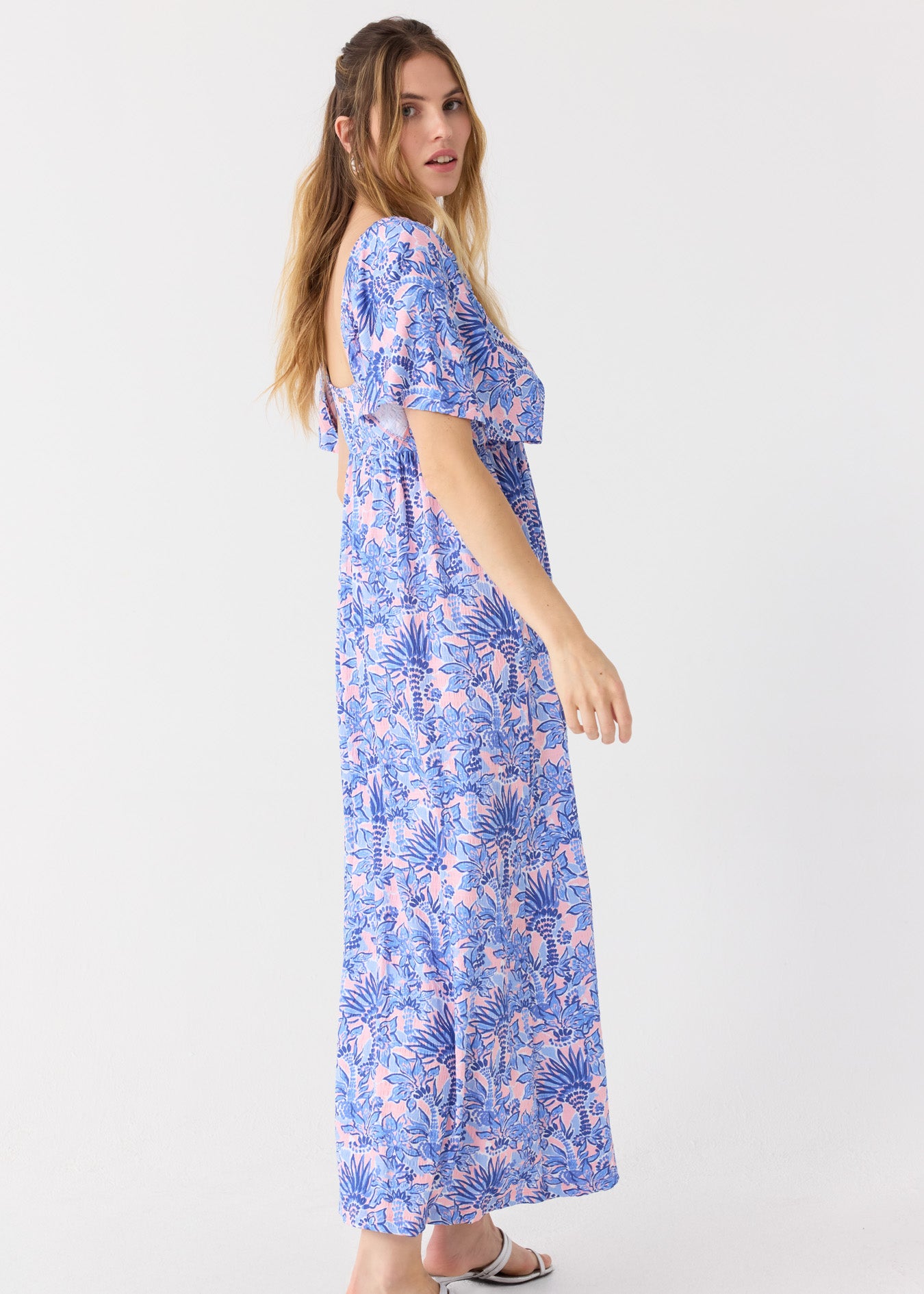 The side of a blonde woman wearing the Cabana Life sun protective Palm Beach Flutter Sleeve Maxi Dress with silver sandals.