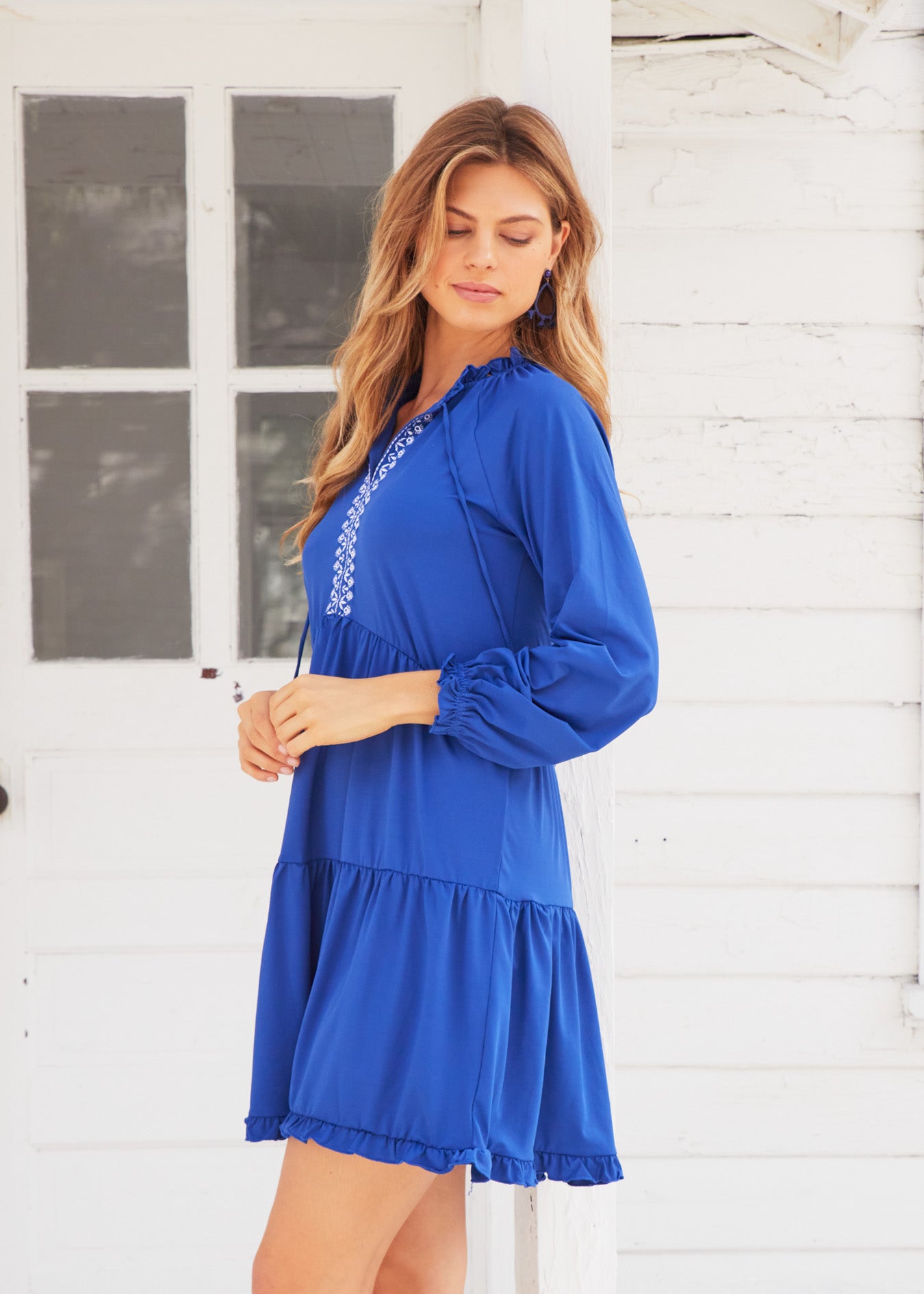 Blonde woman with wavy hair wearing Navy Embroidered Tiered Dress, in front of white building.