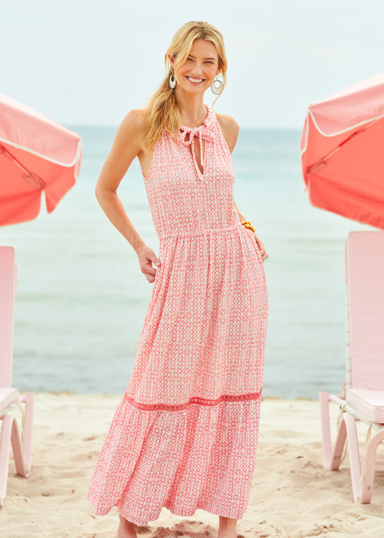 Blonde woman wearing Algarve Halter Maxi Dress on the beach, paired with white earrings and gold jewelry.