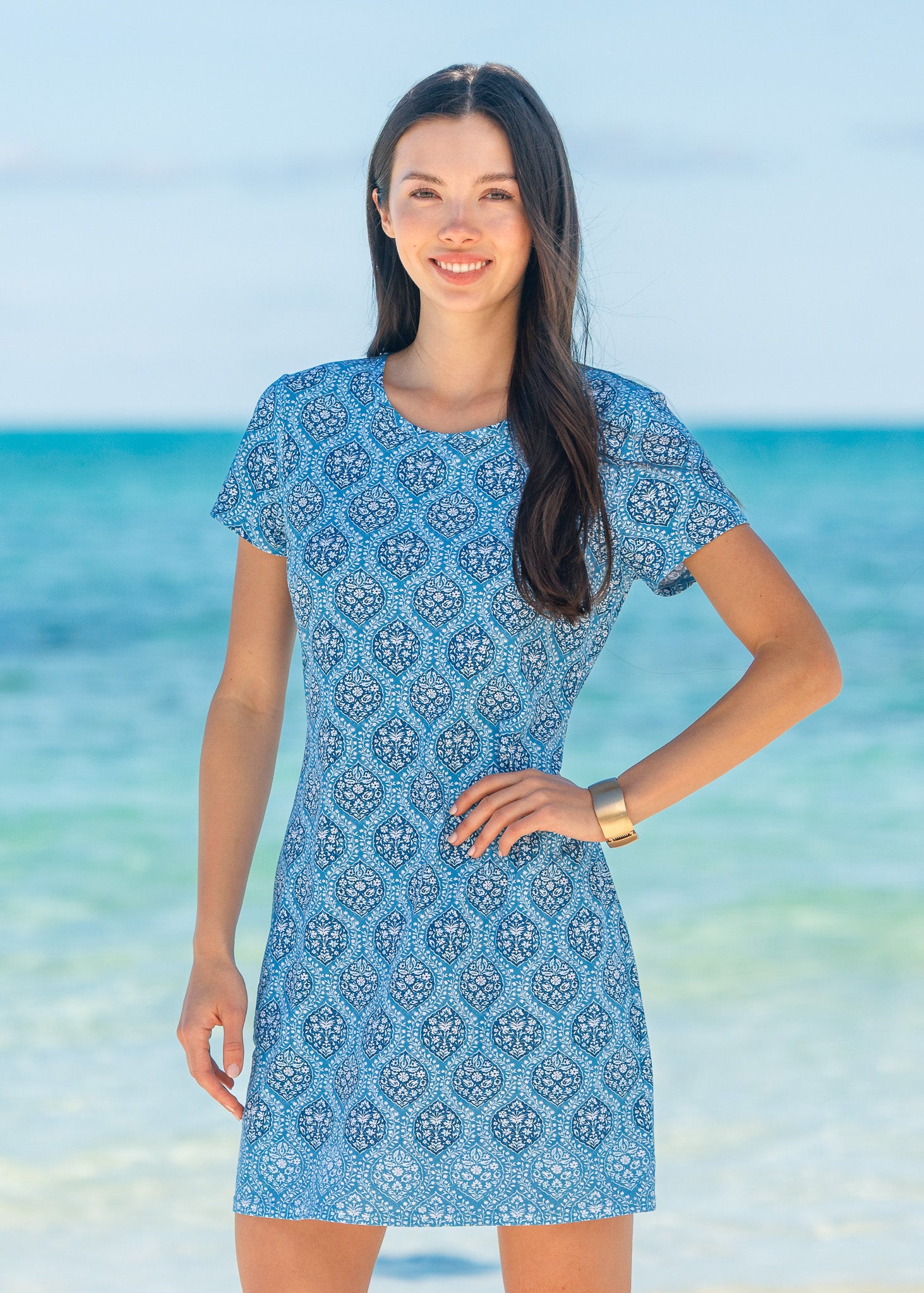 Woman wearing a blue patterned dress standing on a beach with ocean in the background