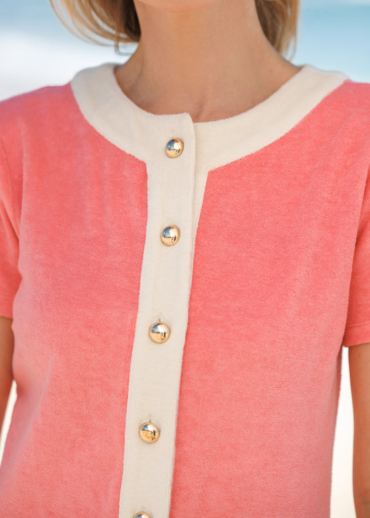 Woman wearing a pink terry dress with gold buttons against a blue sky background