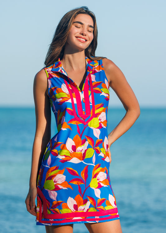 Woman wearing a colorful floral dress standing by the ocean.