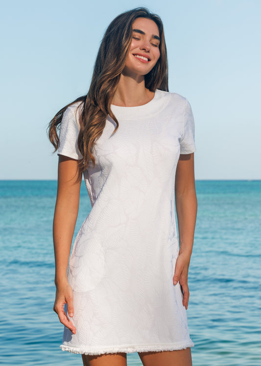 Woman in a white dress standing by the ocean with a clear blue sky.