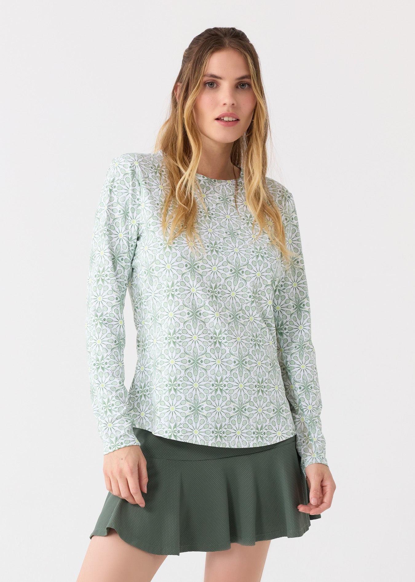 A blonde woman wearing the Cabana Life sun protective Tennis Long Sleeve Performance Top and Olive Green 15" Flounce Skort.