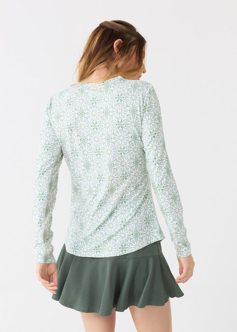 The back of a blonde woman wearing the Cabana Life sun protective Tennis Long Sleeve Performance Top and Olive Green 15" Flounce Skort.