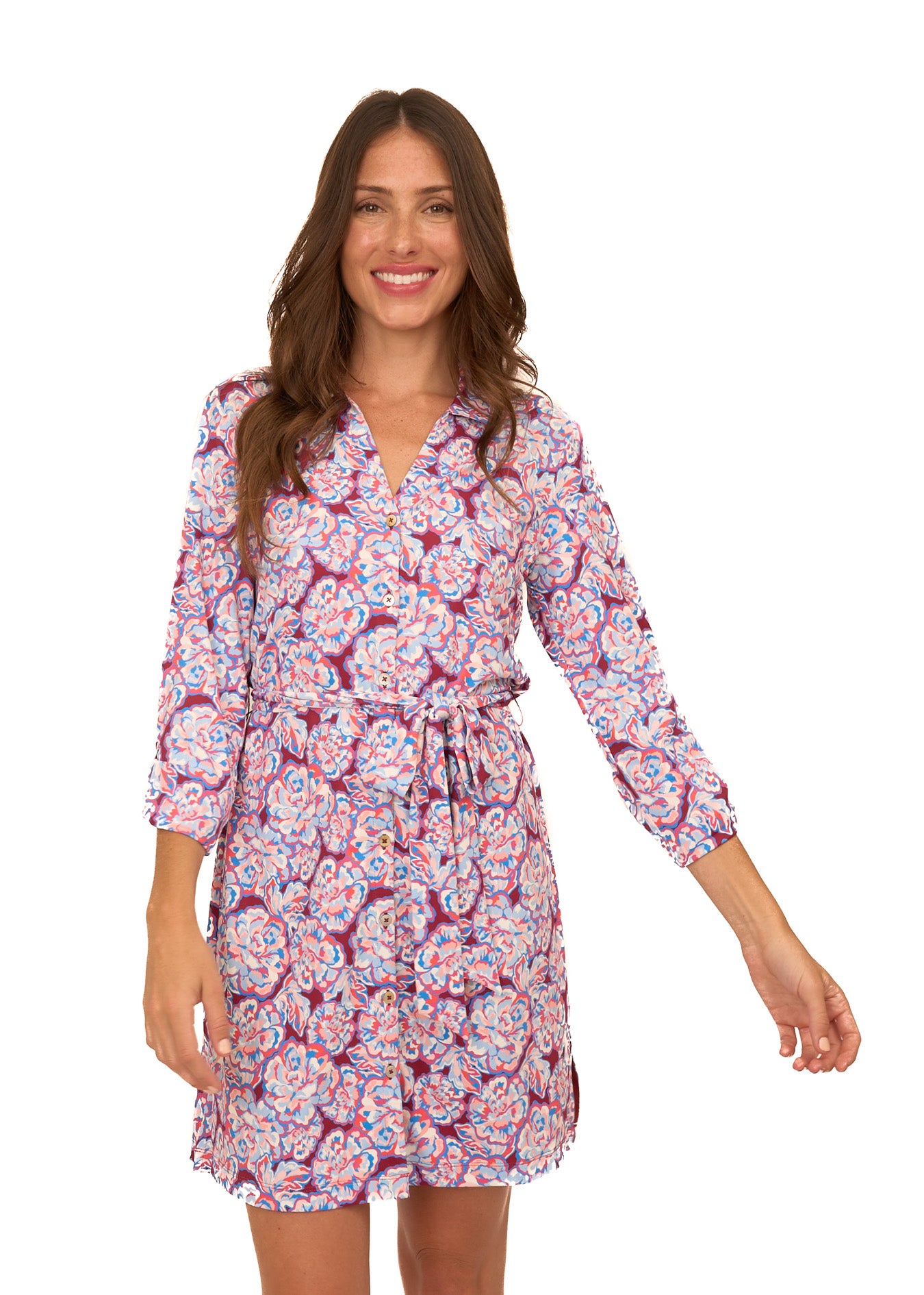 A brunette woman wearing Cabana Life's sun protective Camden Peony Button Down Shirt Dress with sleeves buttoned at a 3/4 length on a white background.