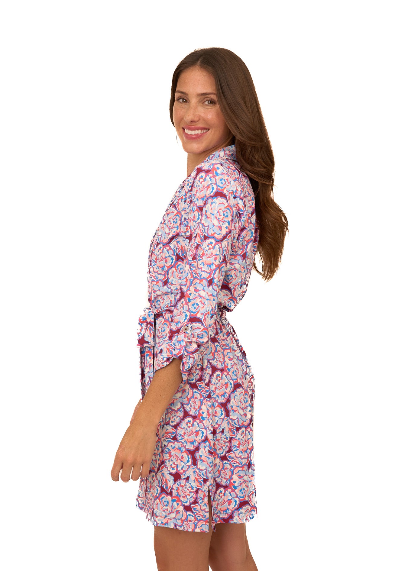 The side of a brunette woman wearing Cabana Life's sun protective Camden Peony Button Down Shirt Dress with sleeves buttoned at a 3/4 length on a white background.