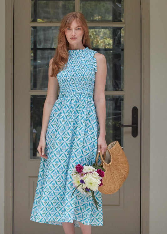 Woman wearing our Rosemary Beach Smocked Maxi Dress holding a basket of flowers outside of a house.