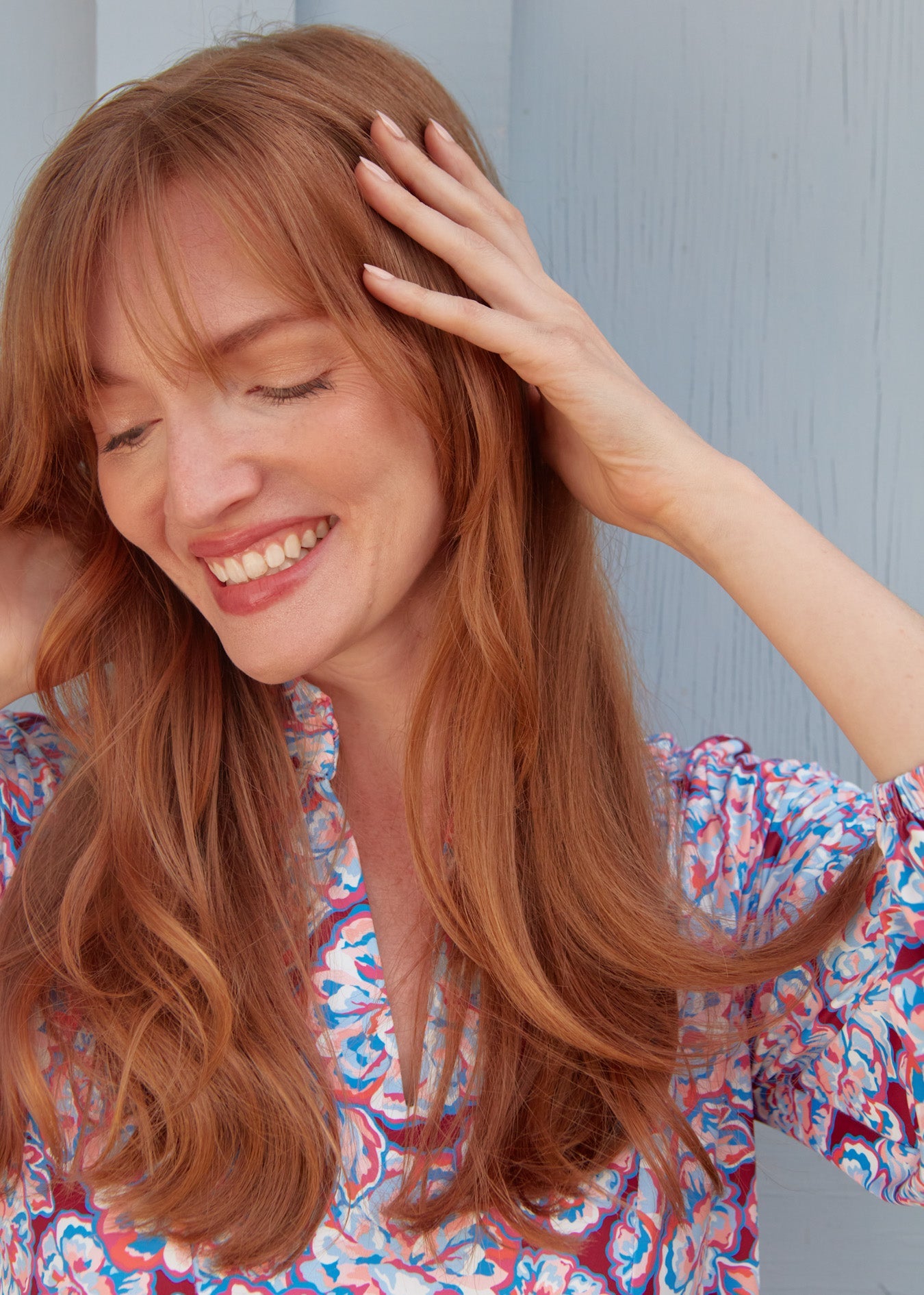 A closeup of a redhead woman touching her hair and head while wearing the sun protective Cabana Life Camden Peony Relaxed Dress.