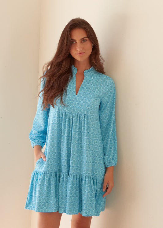 A brunette woman wearing the Cabana Life sun protective Rosemary Beach Relaxed Dress against a wall with a hand in her pocket.