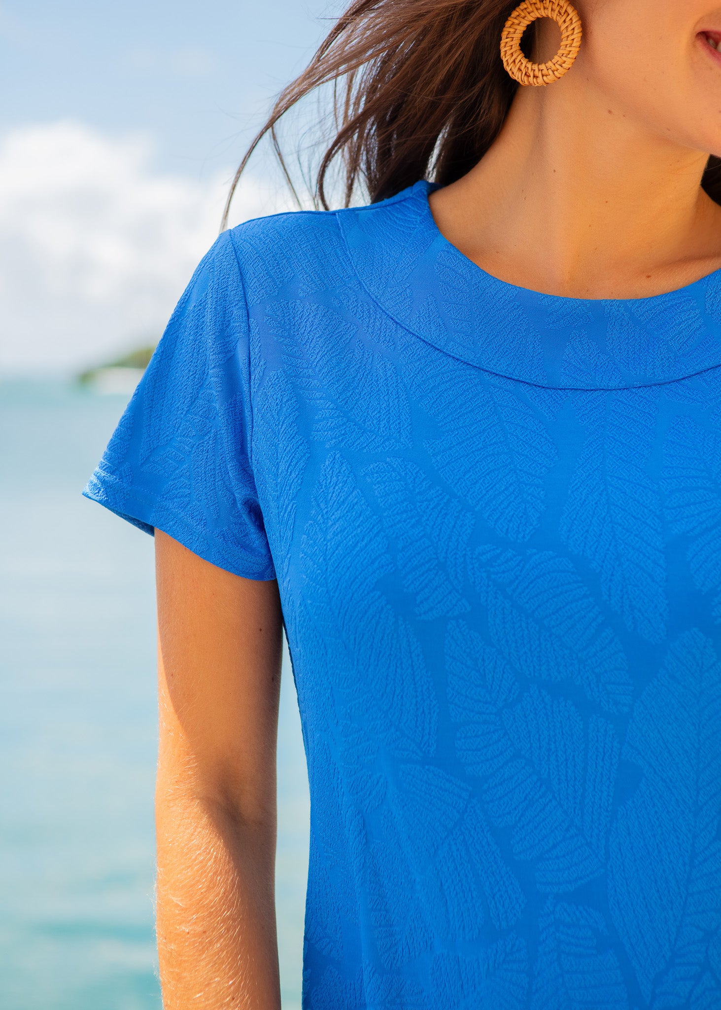 Person wearing a blue shirt with a blurred background of water and sky