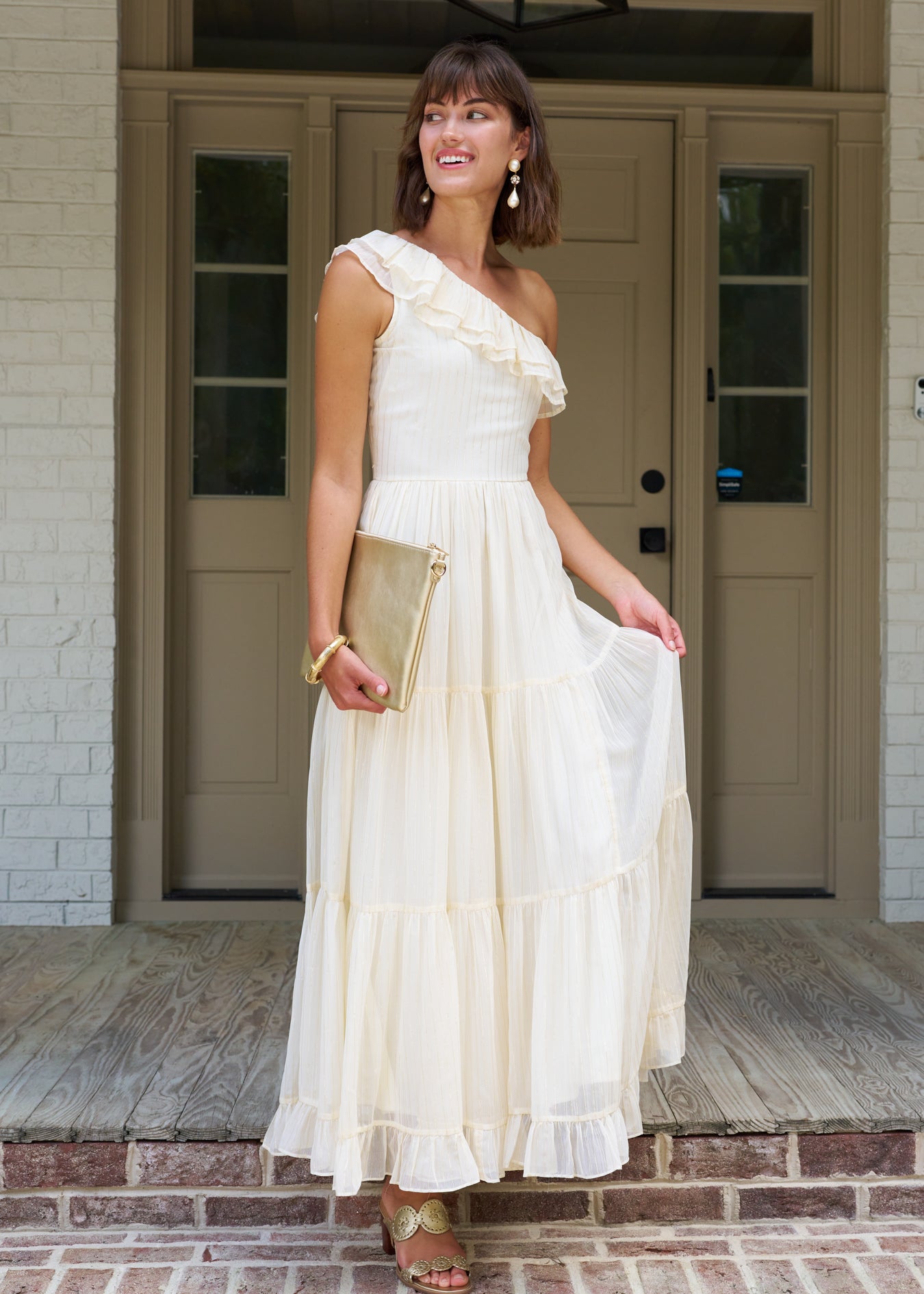 Woman looking to the side wearing the ivory and gold metallic one shoulder maxi dress.