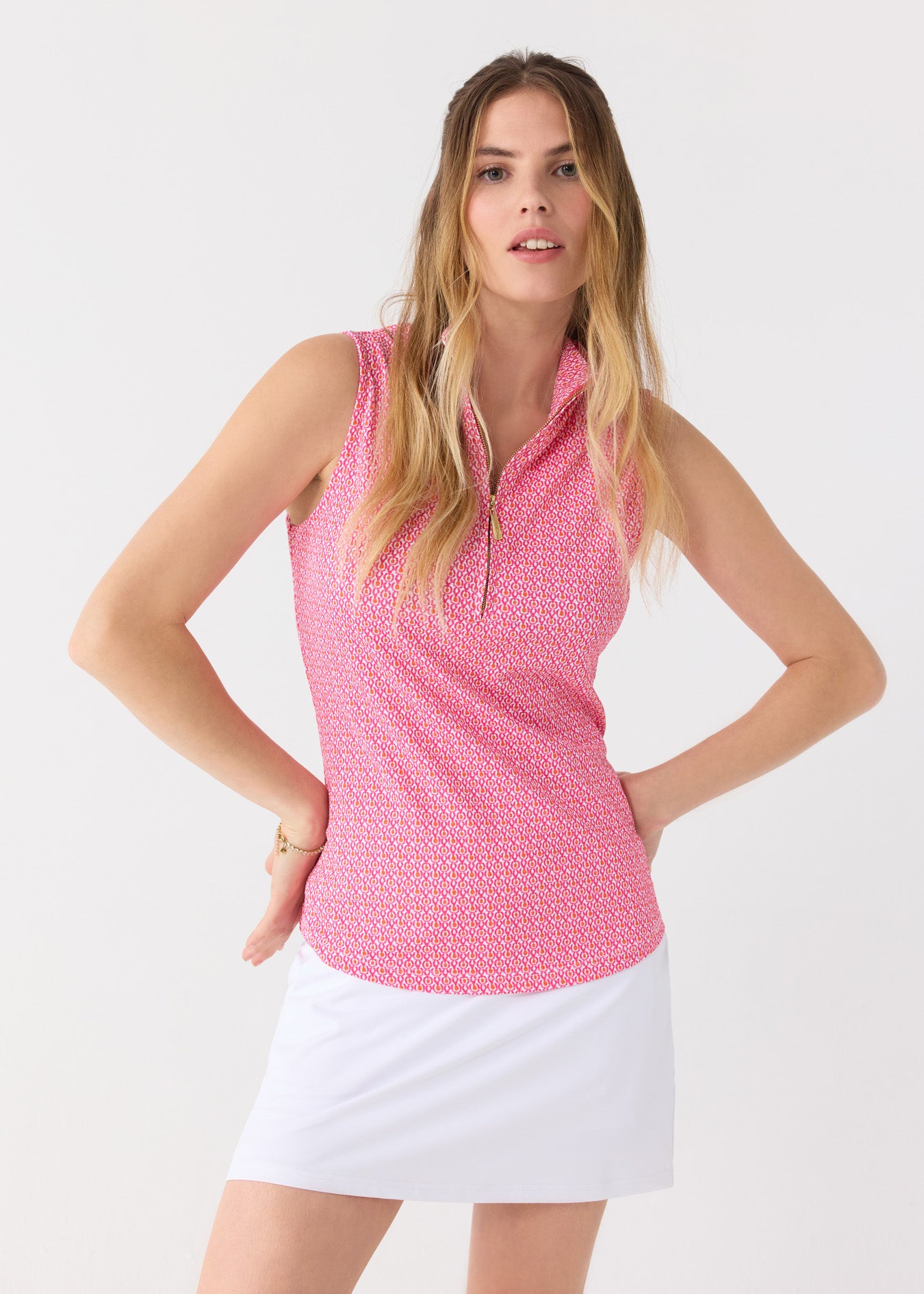 A blonde woman with hands on her hips wearing the Cabana Life sun safe Amelia Island 1/4 Zip Sleeveless Sport Top with a White 15" Skort.