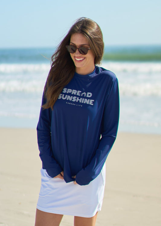 A woman looking down wearing the Navy Spread Sunshine Unisex Performance Shirt and White Skort on the beach.