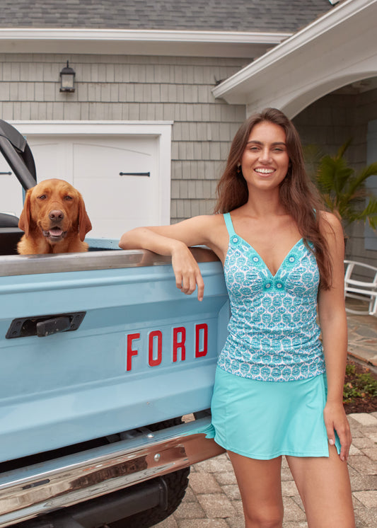 A brunette woman wearing the Cabana Life sun protective Rosemary Beach Embroidered Tankini Top by a blue Ford Bronco.