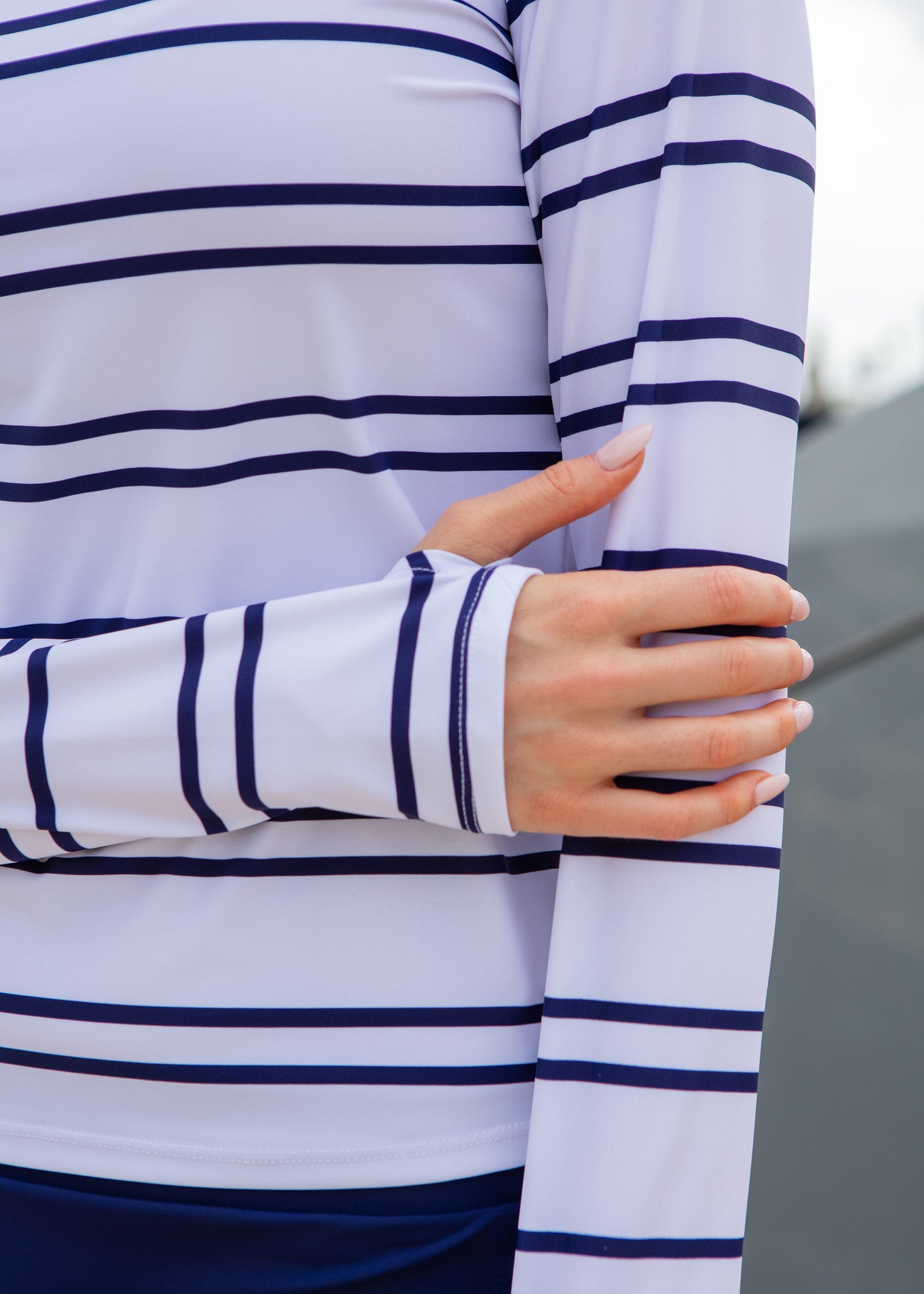 Close-up of a person wearing a white long-sleeve shirt with navy stripes, holding their arm.