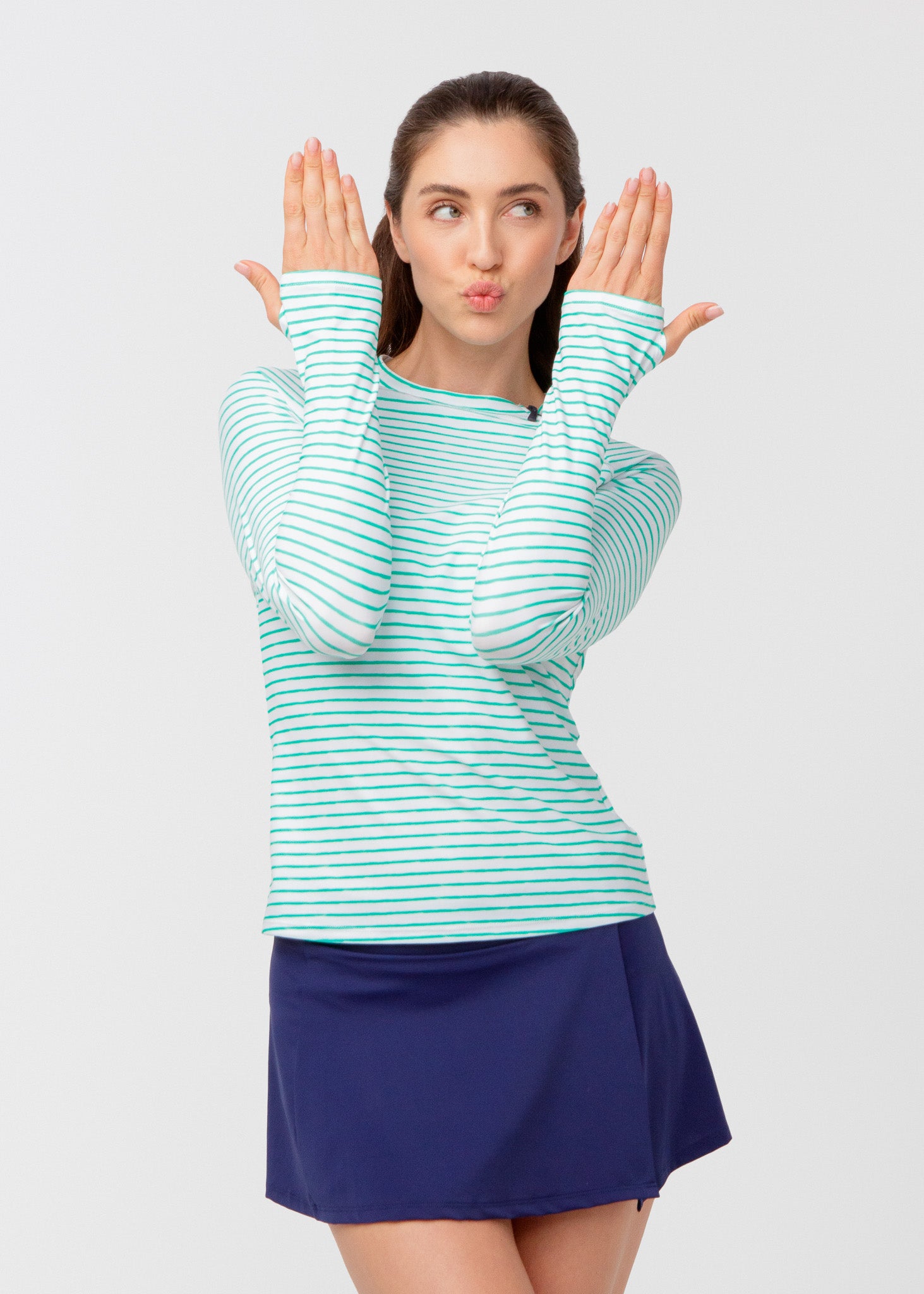 Woman wearing a green and white striped long-sleeve shirt and blue swim skirt on a light gray background