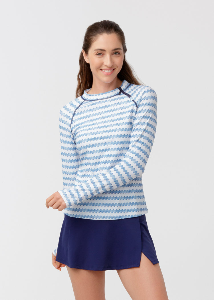 Woman wearing a blue and white striped long-sleeve top and navy skirt on a light gray background