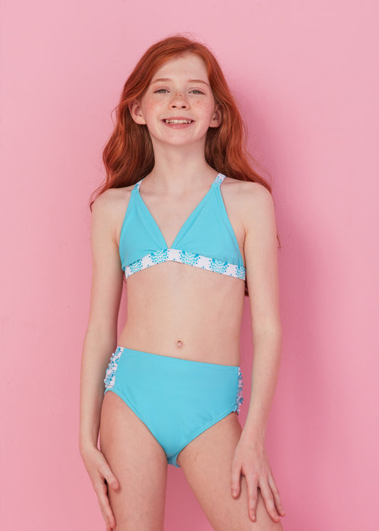 Redhead girl wearing blue bikini set from Girls Amalfi Coast 3-Piece Long Sleeve Rashguard Set in front of pink wall