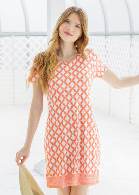 Woman wearing an coral and white patterned dress against a white background