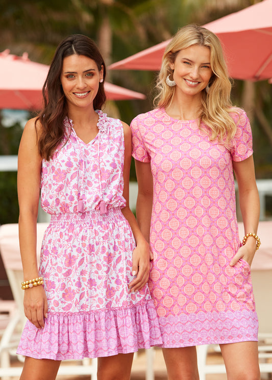 Women standing in front of pink umbrellas with brunette wearing Provence Smocked Waist Dress and blonde wearing the Provence Short Sleeve Shift Dress with her hands in the pockets.
