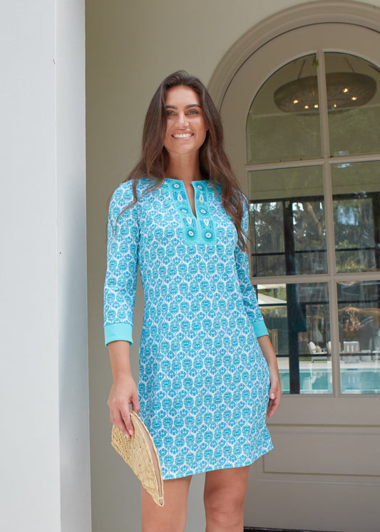 Woman wearing a blue patterned dress standing in front of a glass door.