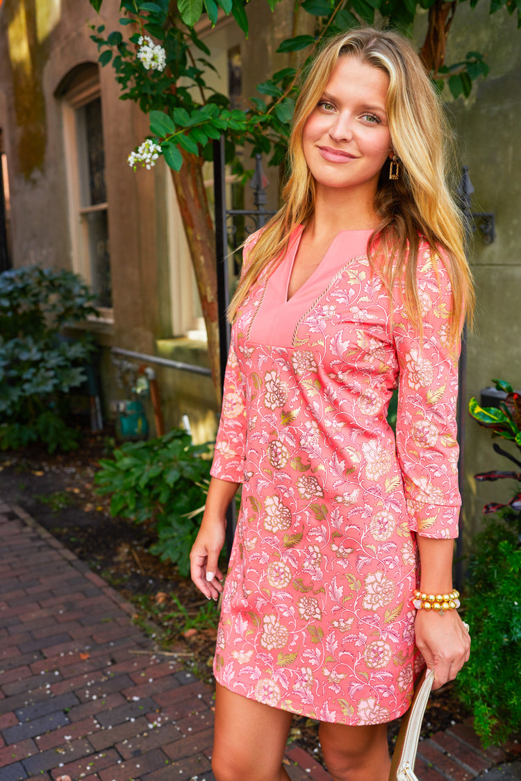 Blonde woman wearing Coral Metallic Tunic Dress in brick alleyway with gold accessories.