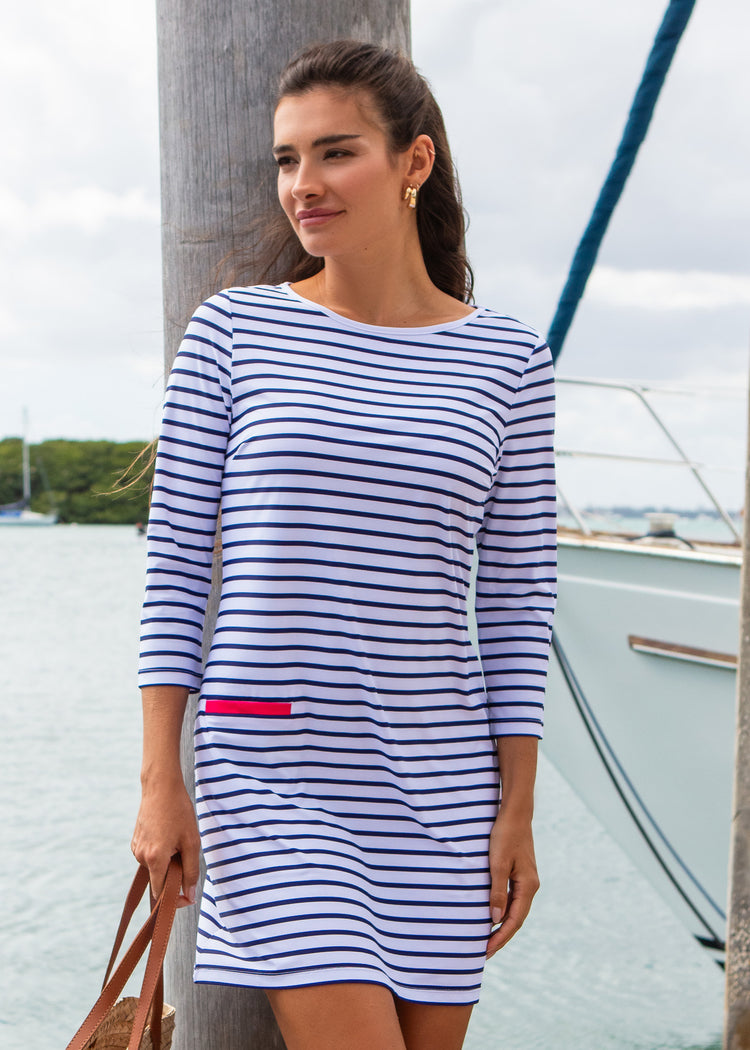 Woman wearing a blue and white striped dress on a dock with water and sky in the background
