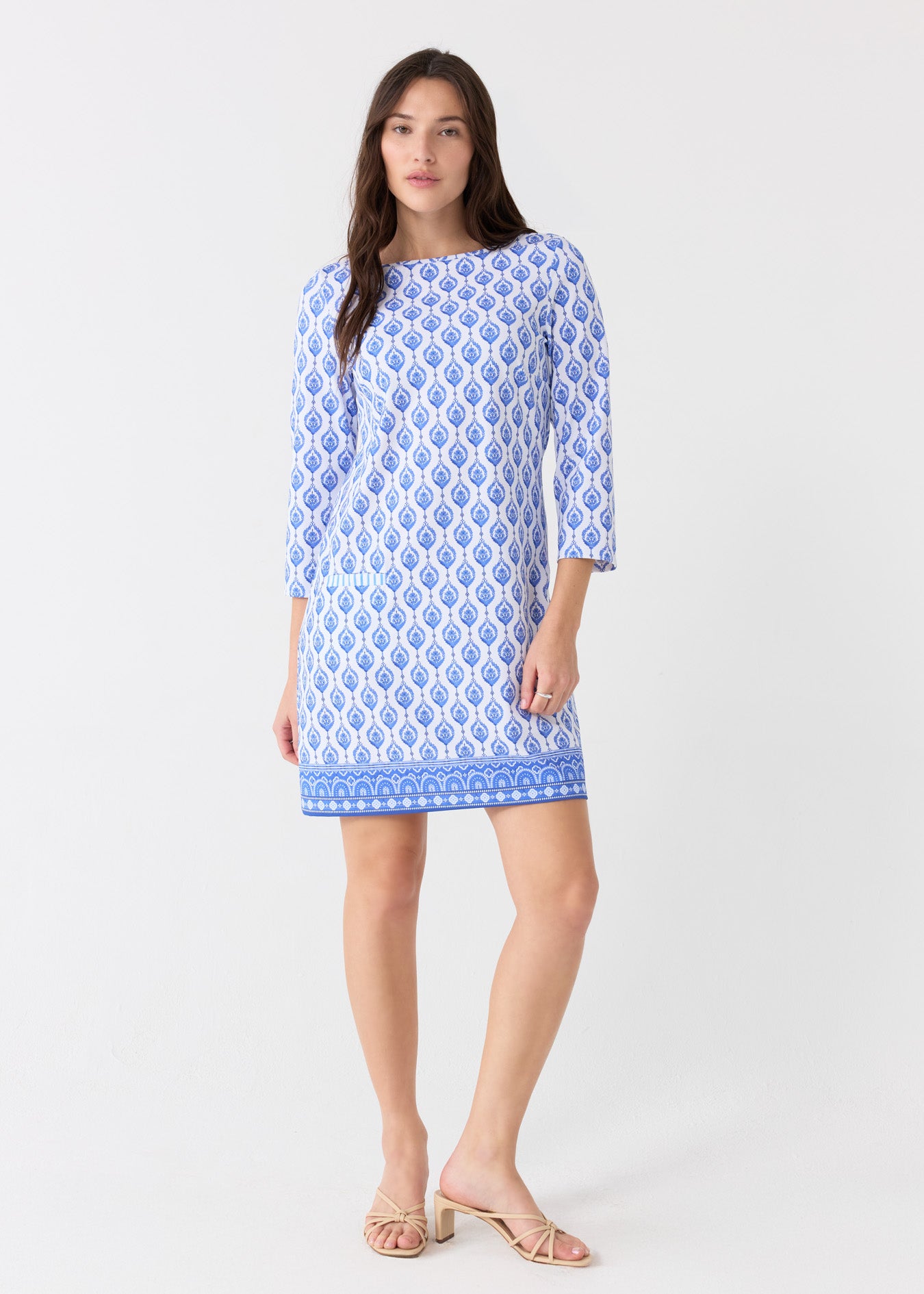 A brunette woman wearing the Cabana Life sun protective Palm Beach Cabana Shift Dress with nude sandals.