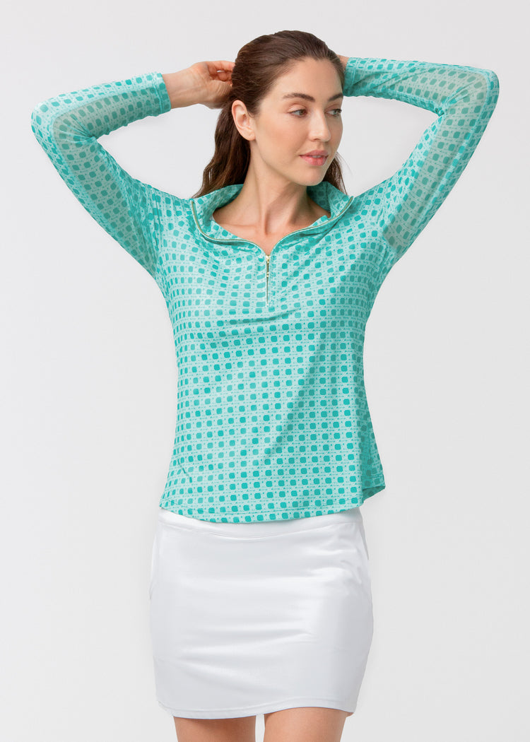 Woman wearing a green basketweave shirt and white skirt on a light gray background