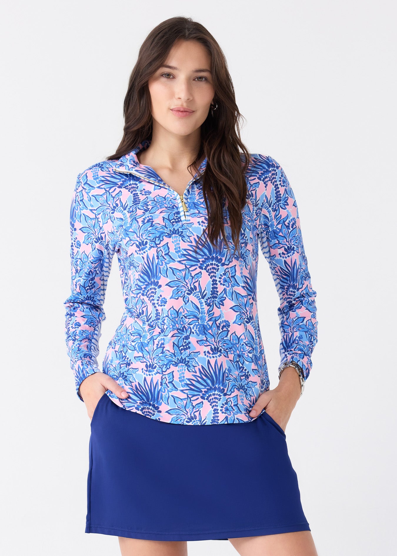 A brunette woman wearing the Cabana Life sun protective Palm Beach 1/4 Zip Sport Top with striped mesh underarms and the Navy 17" Skort.